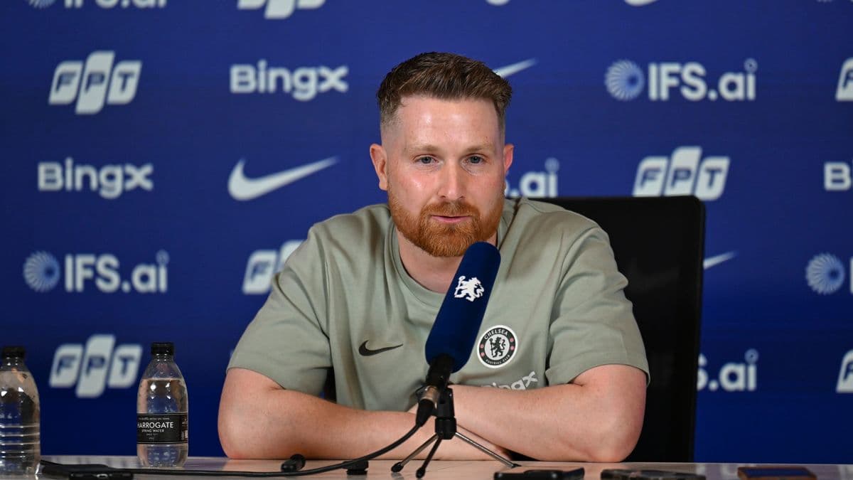 Man speaking at press conference with Chelsea logo