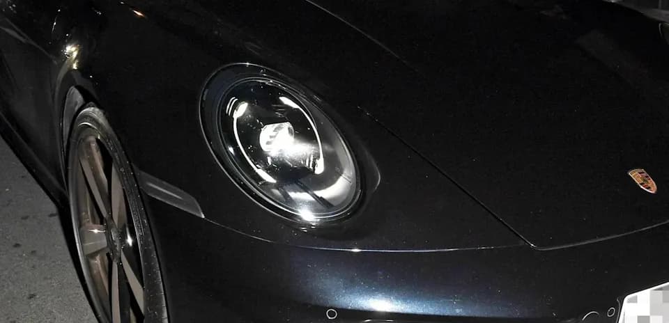 Two men inside a black Porsche at night