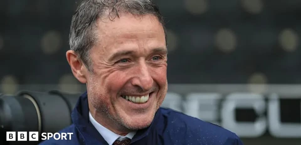 Man smiling in a raincoat at a stadium