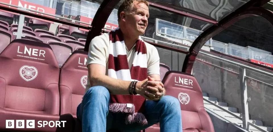 Manager seated in stadium dugout wearing team scarf