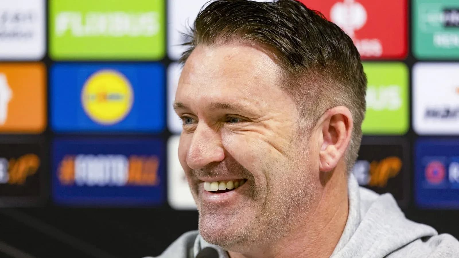 Manager smiling during press conference with sponsors backdrop