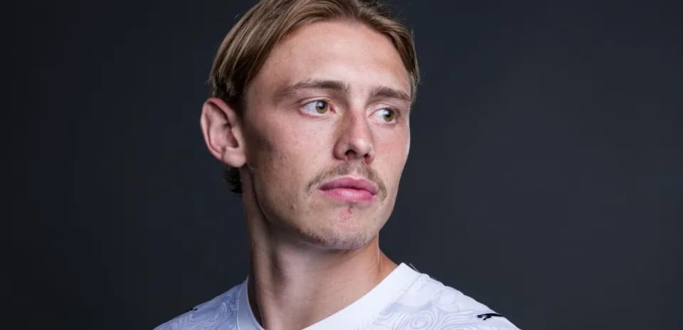 Player posing in a white jersey against dark background
