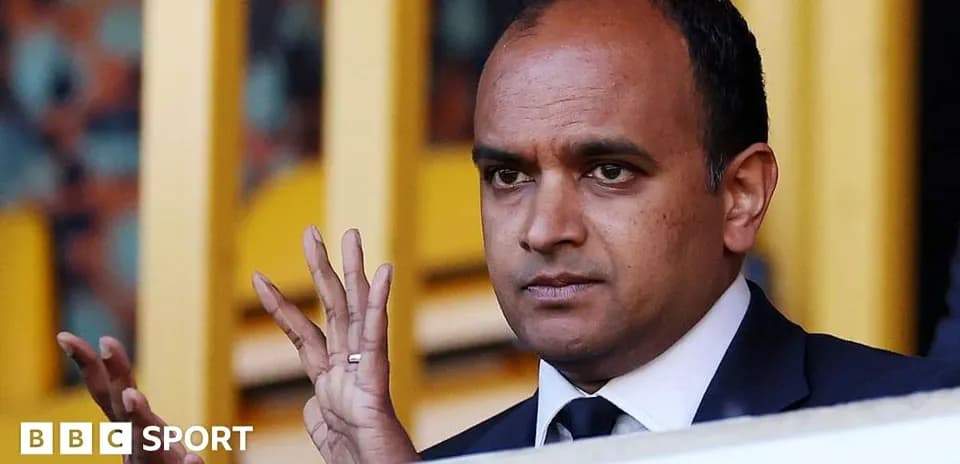 Man gesturing while seated in stadium box