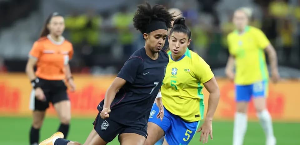 US player dribbling past Brazilian defender during match