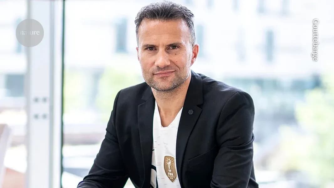 Man in black blazer seated indoors, looking at camera