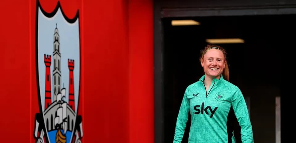 Player in green training kit smiling near club logo