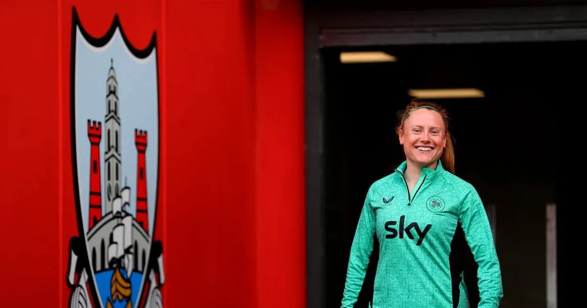 Player in green training kit smiling near club logo